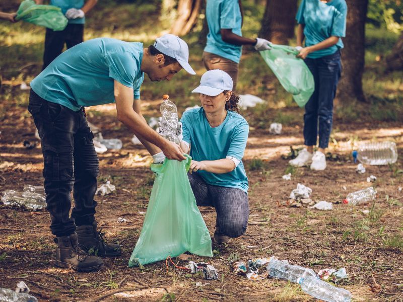Voluntarios de una plantilla recogiendo residuos en bolsas entre los árboles